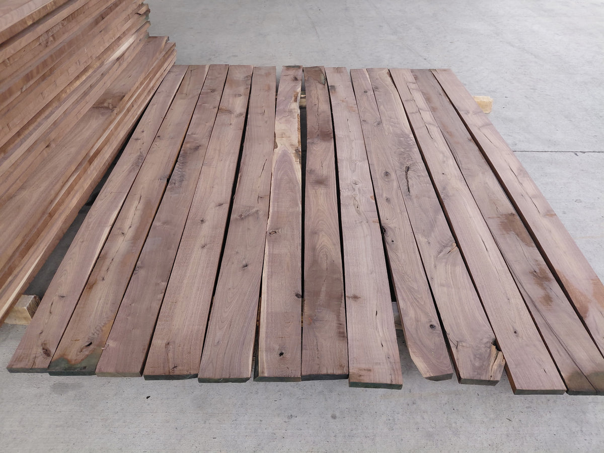 A stack of raw walnut wooden planks with natural grain and knots, arranged on a concrete floor.