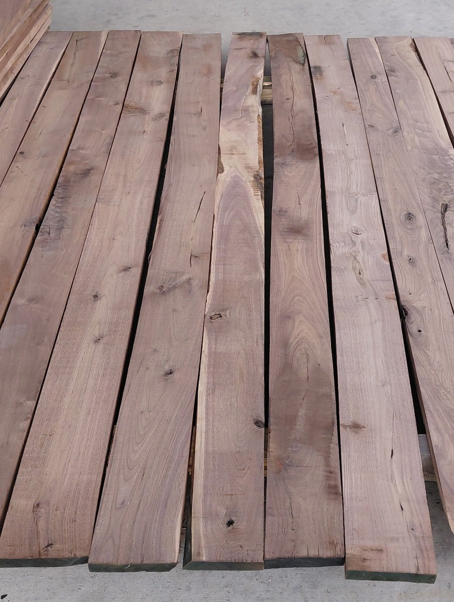 A stack of raw walnut wooden planks with natural grain and knots, arranged on a concrete floor.